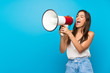 © luismolinero - Young woman over isolated blue background shouting through a megaphone