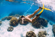 © artifirsov - Free diver young girl with yellow fins glides over sandy bottom and corals.