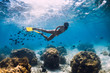 Free diver girl glides with school of fishes in blue sea