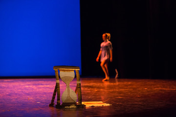 Cardboard hourglass on a theater stage with a blurred figure of a woman in the background