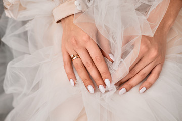 close-up of the hand of a bride who sits clasped hands in a delicately pink dress with a ring on her finger