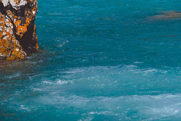 Rock on shore of blue sea. Turquoise mountain lake, the surface of river