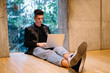 © GalakticDreamer - Handsome young male using laptop and sitting on floor against window