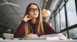 © GalakticDreamer - Charming female blogger in eyeglasses thoughtful looking in cafe window while listening music via headphones, young dreaming hipster girl studying learning course via audiobook and earphones