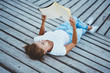 © GalakticDreamer - Young female student reading literature outdoors spending time on hobby outdoors, trendy stylish hipster girl 20s wear in white t-shirt and jeans enjoying learning lying with book at wooden pier