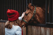 Horse eyes in focus. Horse look. Girl and horse. Girl in red hat. Young girl touching the head of a horse. Concept about love between people and animals. Focus on pet face. 