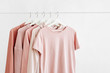 Feminine clothes in pastel pink color on hanger on white background. Spring cleaning home wardrobe. Minimal fashion concept.