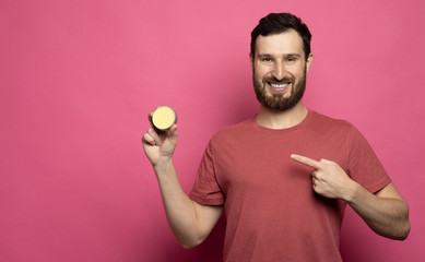 Wall Mural - Close-up image of handsome bearded man holding beard balm on pink background.