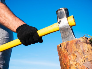 An ax in a man’s hand, stuck in a log, against a blue clear sky on a sunny summer day.