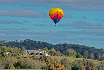 A single hot air balloon flies over a green valley.