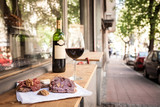 Fototapeta  - Glass and bottle of French red wine on display on the table of a terrace of Paris with slices of baguette bread, brie cheese and saucisson (a cured meat from France) for appetizers