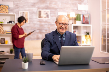 Successful elderly person in suit working on a laptop from home