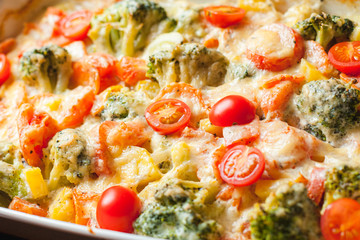 Close up of ready-made baked vegetables in a white ceramic bowl with grated cheese and tomatoes. Natural style