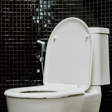 White Toilet Bowl In The Bathroom With Black Tile Wall At Home.