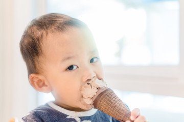 Wall Mural - Happy Little asian baby boy eating chocolate soft cream or ice cream cone at home in summer