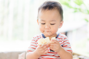 Wall Mural - Happy Little asian baby boy eating jam roll at home in summer.Concept for dessert in meal and happy hungry face in food.