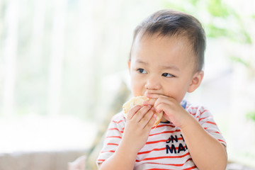 Wall Mural - Happy Little asian baby boy eating jam roll at home in summer.Concept for dessert in meal and happy hungry face in food.