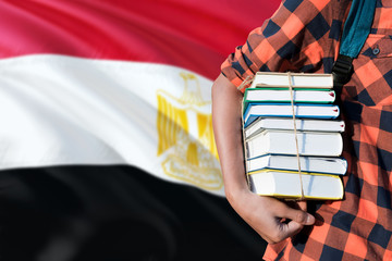 Egypt national education concept. Close up of teenage student holding books under his arm with country flag background.