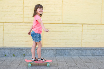 Wall Mural - Cute girl is engaged in a skateboard on a background of a yellow wall. Sport lifestyle.