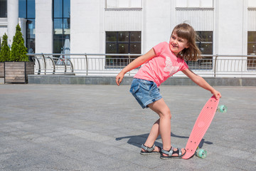 Wall Mural - Little girl learns to skateboard on a sunny day outdoors. Lifestyle.