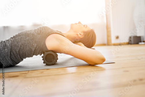 Young woman doing yoga lying on massager on rug in gym during day