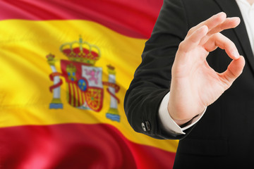 Wall Mural - Spain acceptance concept. Elegant businessman is showing ok sign with hand on national flag background.