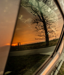 Wall Mural - Sunset, trees and fields reflecting on the car window.