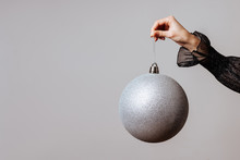 White Christmas Ball In Female Hand On Grey Background