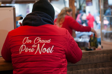 portrait on back view of people giving traditional food at the christmas market with text on vest vin chaud du pre noel traduction in english mulled wine of santa claus