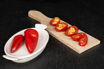 Wall Mural - Group of two whole five slices of pickled red pepper on wooden cutting board on white ceramic plate on grey stone