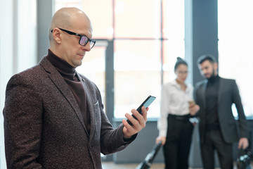 Aufkleber - Serious bald mature businessman in formalwear looking through data in smartphone
