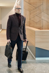 Aufkleber - Bald mature businessman pulling suitcase while moving along reception counter