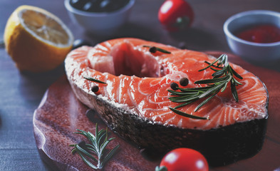 fresh raw salmon steak with tomato, lemon, olive, pepper, sauce and aromatic herbs on the wooden table background