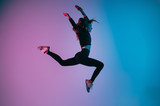 Sporty girl in charismatic jump moment against trendy color background. Young fit dance woman jumping. Studio shot