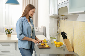 Poster - Young woman cutting lemon for refreshing drink in kitchen