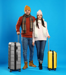 Canvas Print - Happy young couple in warm clothes with suitcases on blue background. Winter vacation