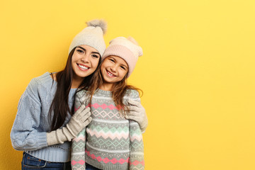 Happy mother and daughter in warm clothes on yellow background, space for text. Winter vacation