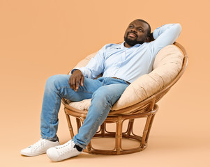 Poster - African-American man relaxing in armchair against color background