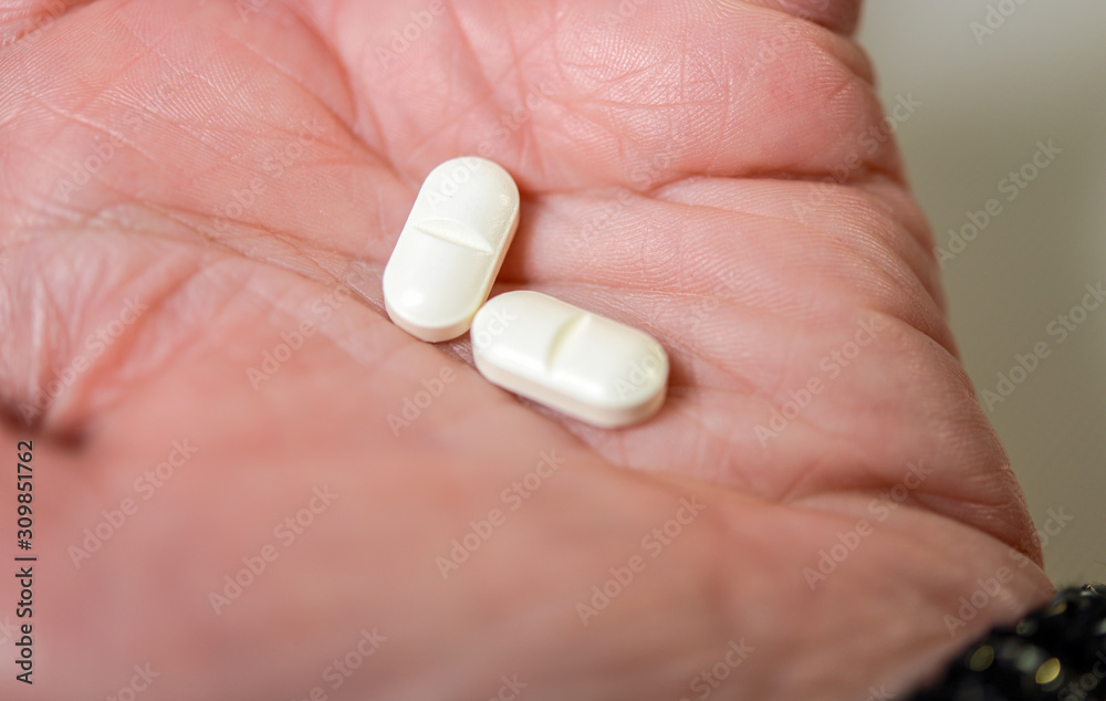 Foto stock di Nahaufnahme: Zwei weiße Tabletten in der Hand einer Frau - selektiver Fokus auf eine Tablette