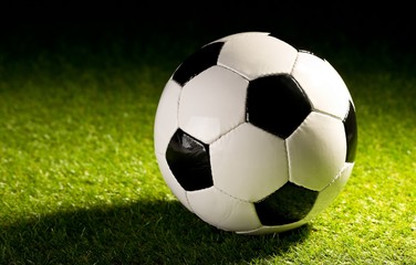 single soccer ball on green grass lawn background with harsh stadium lighting