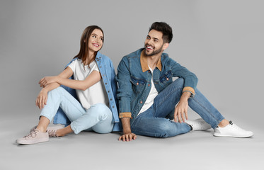 Wall Mural - Young couple in stylish jeans sitting on grey background