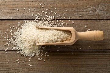 Wall Mural - White uncooked, raw long grain rice in wooden scoop on brown wooden table top view flat lay from above