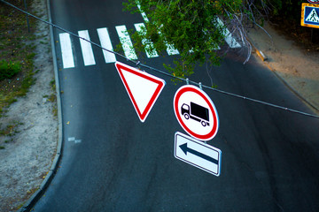 Traffic signs on a wire over the road. A sign obliging to give way. And forbidding the passage of trucks.