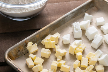 Close up on a baking sheet of butter and shortening, beside a bowl of flour