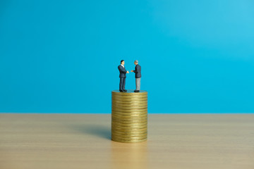 Miniature business concept - two businessman make an handshake for partnership agreement handshake with coin stack