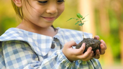 Happy asian girl holding young plant at garden.