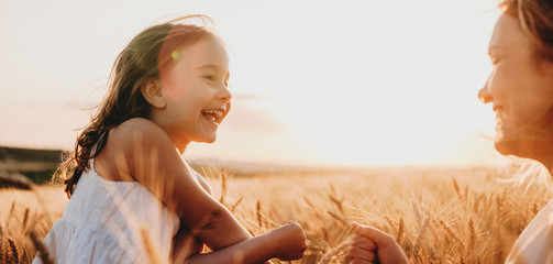 Wall Mural - side view portrait of a happy little girl laughing while looking at her mother in a field of wheat a
