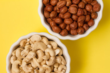 hazelnuts and cashews in two white bowls on a yellow background. the concept of proper nutrition and health. Healthy food and snack, organic vegetarian food. Walnuts, pistachios, almonds,