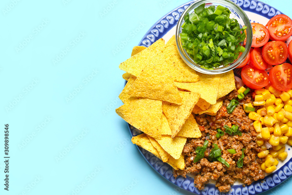 Plate with tasty meat, nachos and vegetables on color background