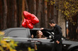 © Pixel-Shot - Man near his girlfriend with air balloons sitting in car. Valentine's Day celebration